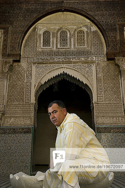 A man wearing traditional Middle Eastern clothing sits in one of the decorative gardens of a mosque.