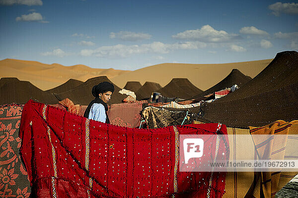 A desert guide in traditional dress walks through a tent camp with brightly colored blankets.