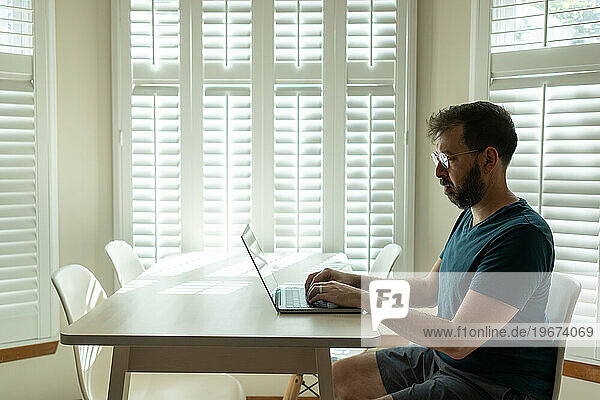 Bearded man in glasses works on laptop
