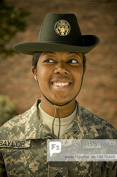 A drill sergeant smiles and looks coil while standing near the barracks of her military trainees.