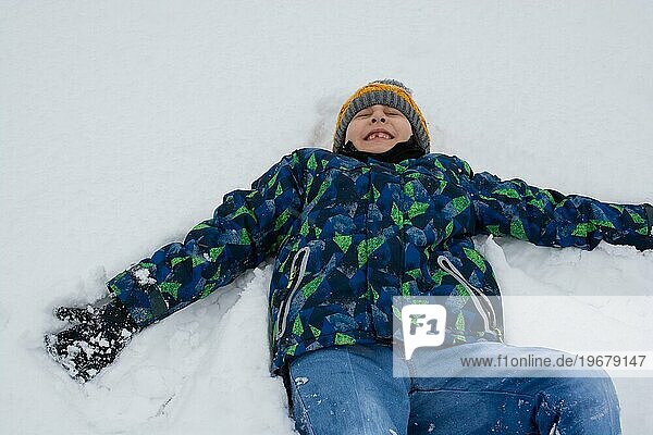 Fröhlicher Junge liegt im Schnee. Aktive Freizeit im Freien für Kinder in der Natur im verschneiten Wintertag