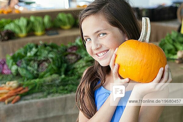 Glückliches junges blauäugiges Mädchen hält einen frischen Kürbis auf dem Bauernmarkt