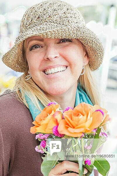 Lächelnde blonde Frau mit Hut  die einen frisch geschnittenen Blumenstrauß auf dem Bauernmarkt hält