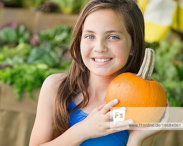 Glückliches junges blauäugiges Mädchen hält einen frischen Kürbis auf dem Bauernmarkt