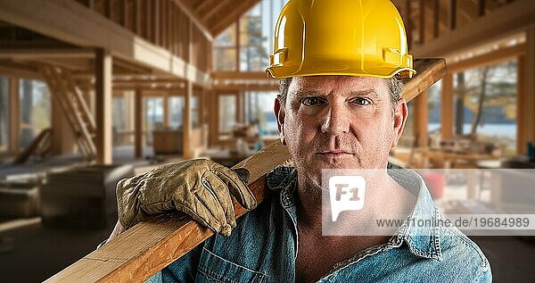 Männlicher Bauunternehmer auf einer Baustelle mit Schutzhelm und Arbeitshandschuhen  der ein 2x4 Holz hält