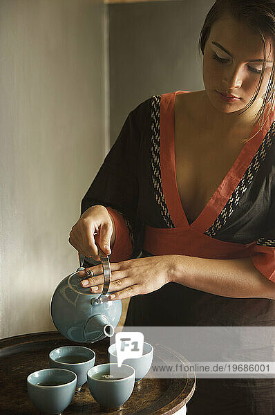 Young woman holding teapot and pouring green tea