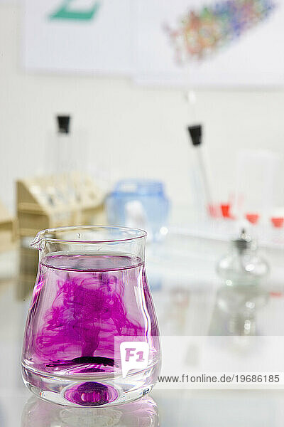Close up of a glass container filled with fluid and dark pink chemical solution