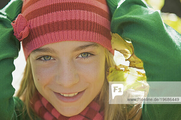 Smiling young girl with her hands on her head wearing a woolly hat