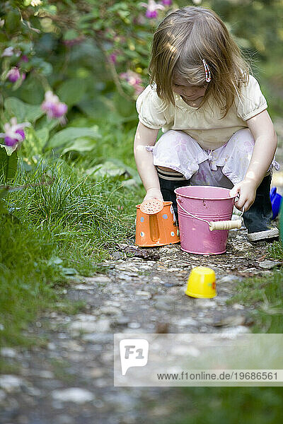 Young girl crouching in a garden playing with gardening toys