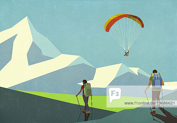 Couple hiking below paraglider in sunny mountains
