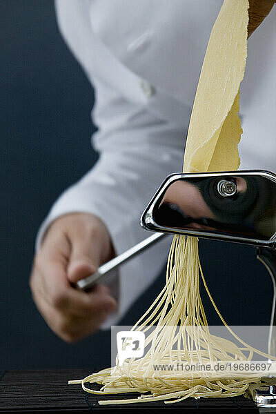 Close up of a chef hand turning the handle of a pasta maker with tagliolini coming out