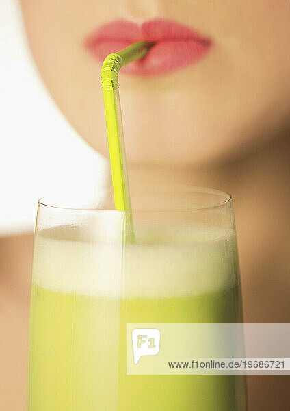 Close up of a woman mouth drinking a vegetable smoothie with a straw