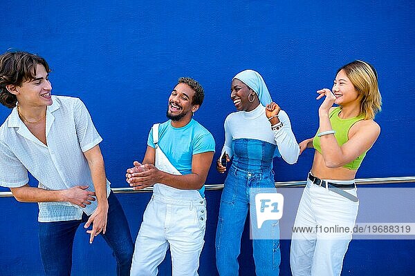 Frontalansicht von vier multiethnischen Freunden  die sich beim Tanzen neben einer blauen Wand amüsieren