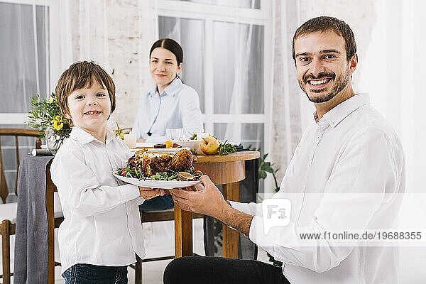 Glücklicher Mann mit Sohn  der einen Teller mit Hühnchen hält