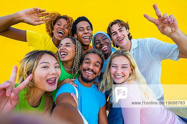 Multiethnische Freunde machen ein Selfie neben einer gelben Wand und gestikulieren dabei Frieden