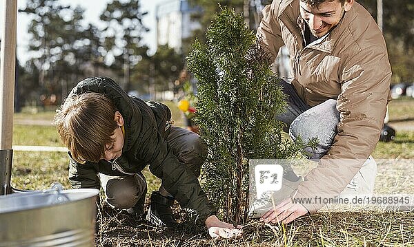 Kleiner Junge und sein Vater pflanzen einen Baum im Freien