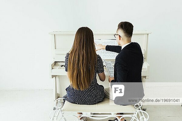 Rückansicht junger Mann unterrichtet seine Freundin am Klavier