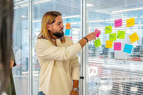 Kreativer junger Mann neben einem Glas mit Haftnotizen  der seinen Kollegen Ideen erläutert