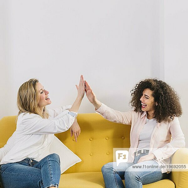 Fröhliche Frauen  die sich auf dem gelben Sofa die Hände reichen