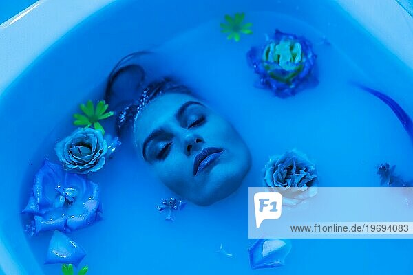 Künstlerisches blau gefärbtes Porträt von oben einer Frau im geblümten Milchbad