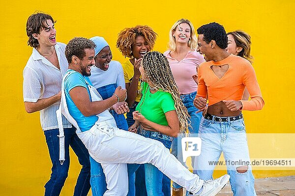 Fröhliche multikulturelle Freunde tanzen und haben Spaß neben einer gelben Wand im Freien
