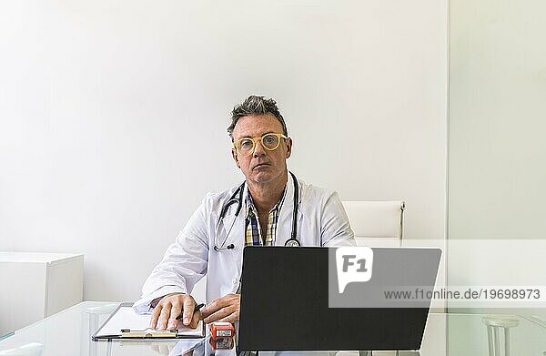 Männlicher Arzt bei der Arbeit in einer Arztpraxis mit Blick in die Kamera