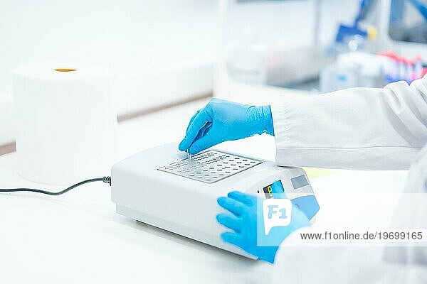Hände eines Biologen mit blauen Latexhandschuhen bei der Arbeit an einer Maschine zur Analyse von Zellen