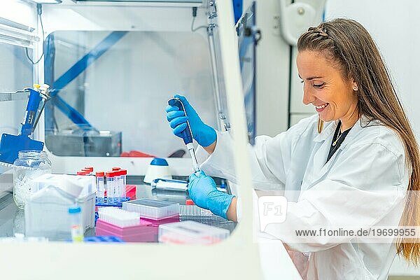 Lächelnder Biologe  der mit einer Pipette Zellen aus einer Schale in einem Labor entnimmt