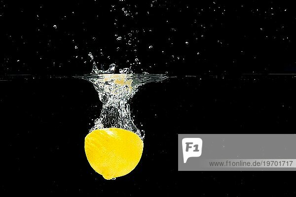 Halbierte Zitrone fällt in sauberes Wasser vor schwarzem Hintergrund