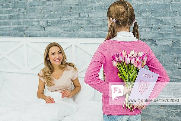 Tochter hält Grußkarte Tulpen Mutter Bett