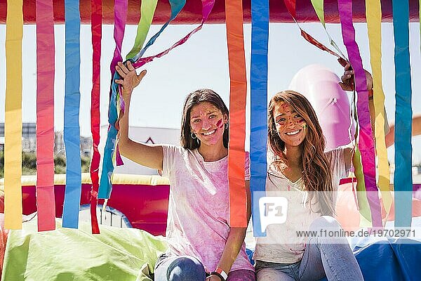 Lächelnde junge Frauen mit Holi Farbe ihr Gesicht suchen Kamera