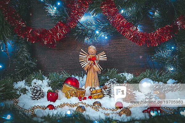 Weihnachtliche Szene  Strohengel mit Geschenkpäckchen in Schnee  Deko  Lichterkette  Holzhintergrund