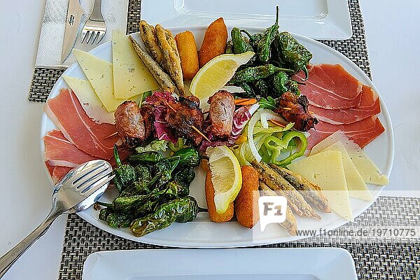 Vorspeisenteller auf gedeckter eingerichtete Tisch mediterranes italienisches Gericht Vorspeise auf großer Teller roher Schinken  Scheiben von Käse  Peperoni  Paprika  an Stäben frittierte Fischchen  Scheiben von Zitrone  international