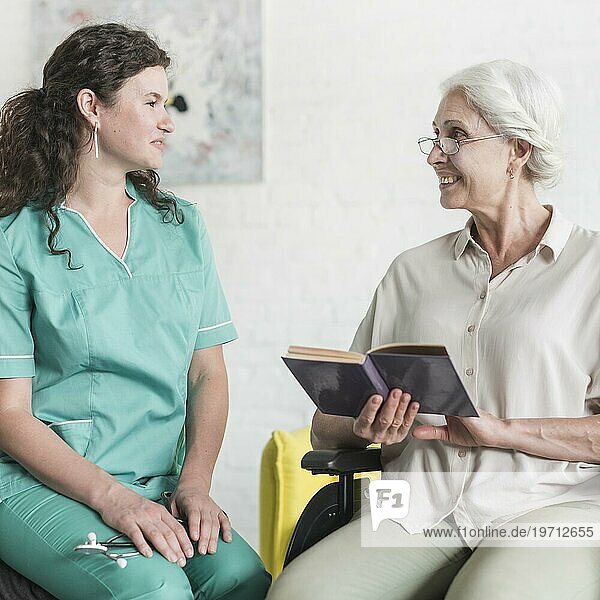 Attraktive Krankenschwester suchen ältere Frau Patientin sitzt Rollstuhl mit Buch