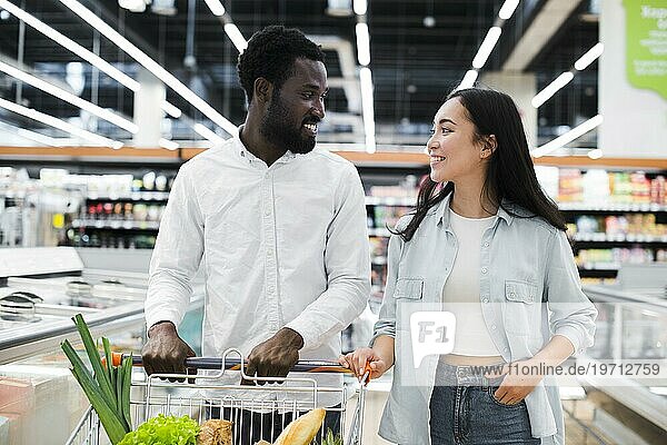 Fröhliches gemischtrassiges Paar mit Einkaufswagen im Supermarkt