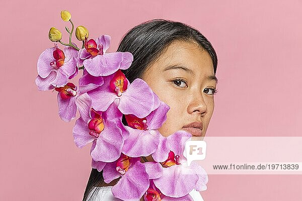 Frau bedeckt ihr Gesicht mit einer Orchidee und schaut in die Kamera