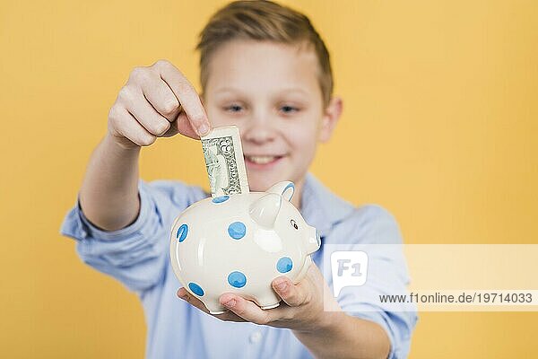 Selektiver Fokus Junge einfügen Geldschein Polka Dot Keramik Sparschwein gegen gelben Hintergrund