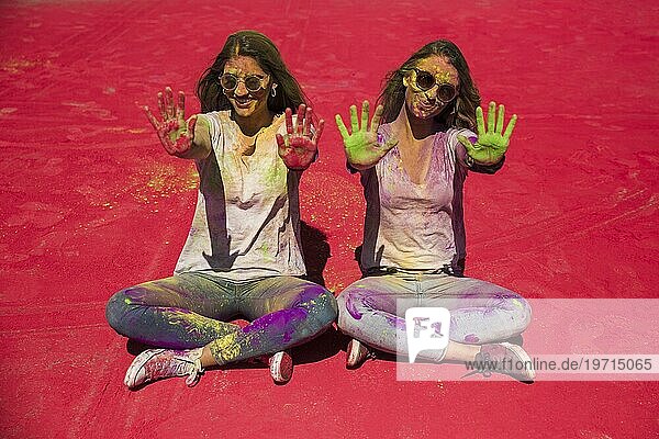 Porträt zweier junger Frauen  die ihre mit Holi Farbe bemalten Handflächen zeigen