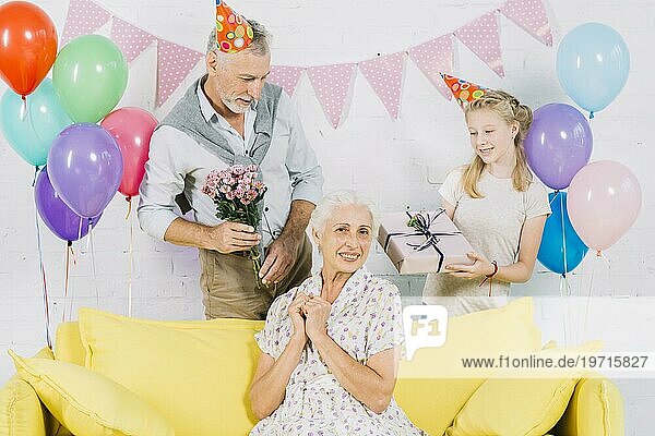 Glückliche Frau sitzt Sofa vor Ehemann Enkelin hält Geburtstagsgeschenke