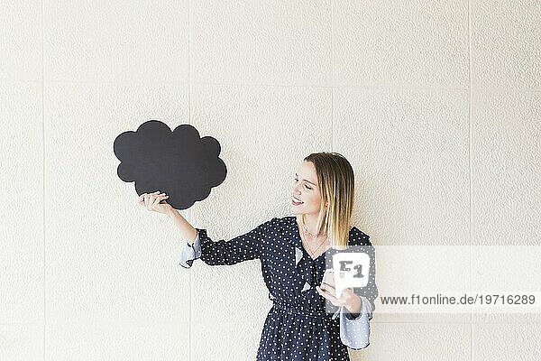 Lächelnde junge Frau hält Mobiltelefon Wolke aus Karton