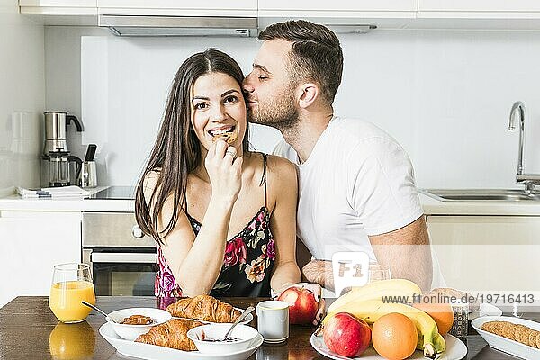Junger Mann küsst ihre Freundin essen Kekse mit Früchten Croissant Tisch Küche