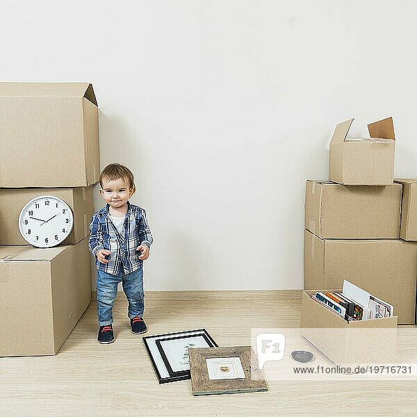 Porträt lächelnder Junge steht in der Nähe von Kartons sein neues Haus