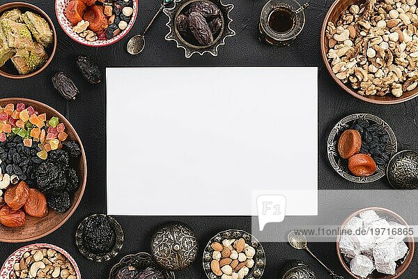 Erhöhte Ansicht leere weißes Papier mit köstlichen getrockneten Früchten Nüsse Süßigkeiten Ramadan schwarz texturierten Hintergrund umgeben