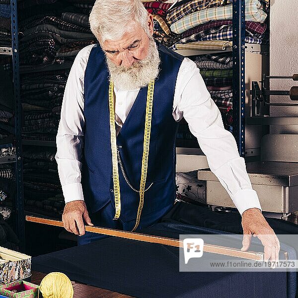 Porträt älterer männlicher Modedesigner  der Stoff mit einem Holzlineal mißt