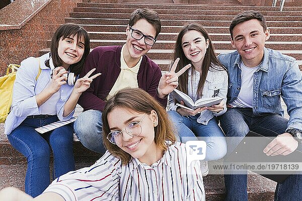 Studenten  die auf Treppen sitzen und mit zwei Fingern in die Kamera schauen