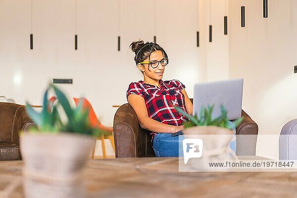 Junge Unternehmerin arbeitet von zu Hause aus mit einem Laptop auf einem bequemen Sofa