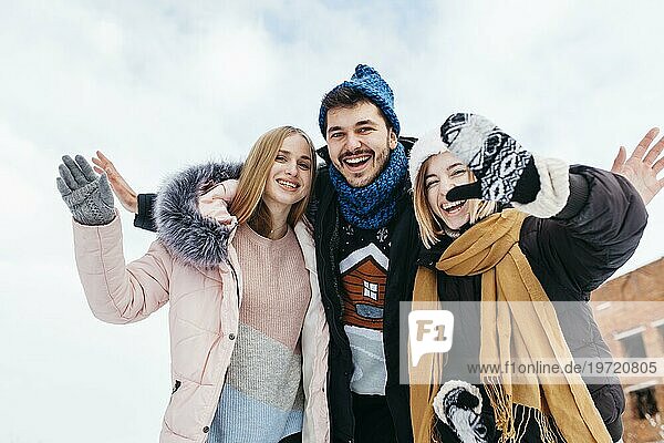 Drei Freunde Winterkleidung winken mit Händen draußen