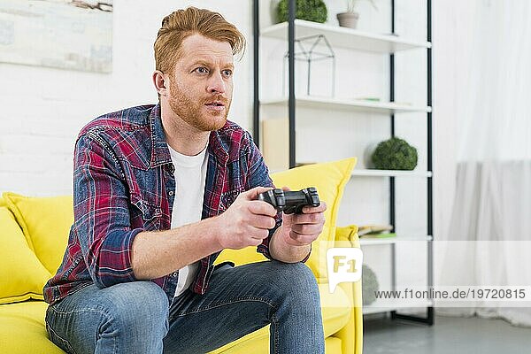 Close up junger Mann sitzt gelbes Sofa spielen Videospiel mit Joystick Wohnzimmer