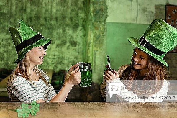 Glückliche Freundinnen feiern gemeinsam den St. Patrick's Day in einer Bar mit Getränk