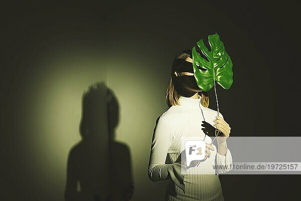 Frau bedeckt Gesicht mit großem grünen Blatt